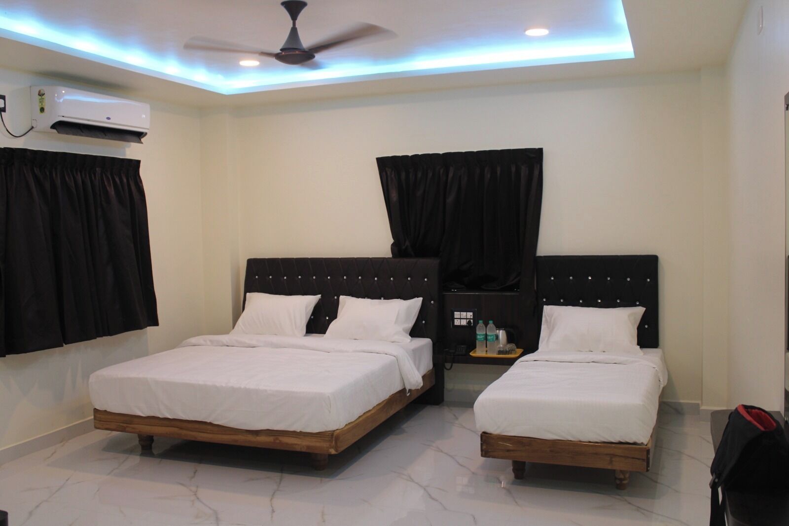 A hotel room with two beds, a ceiling fan, an air conditioning unit, and a small table with bottles.