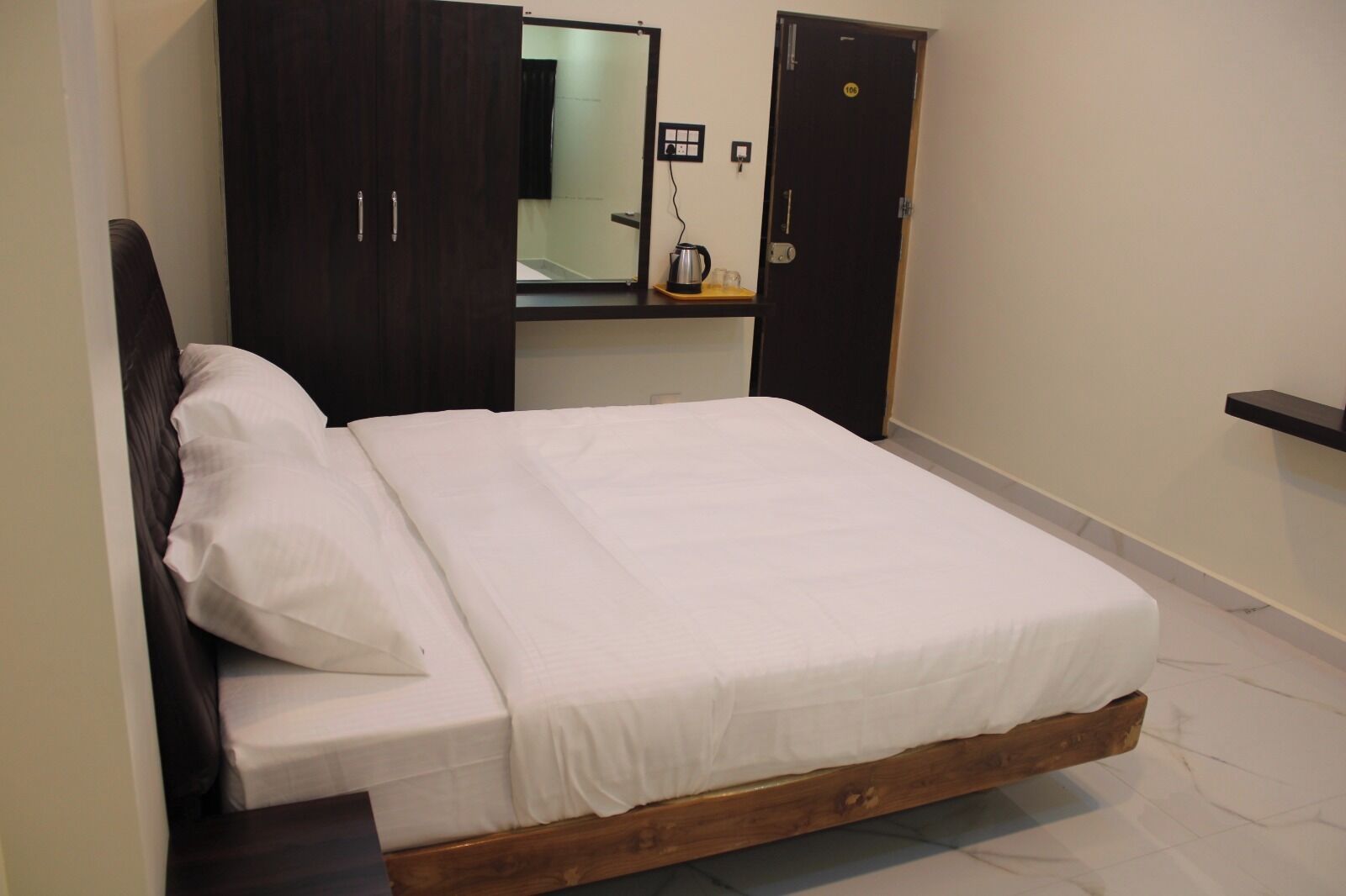 A bedroom with a wooden bed, a dark wardrobe, and a small bedside table with a kettle.