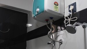A bathroom with a wall-mounted hand dryer, a towel rack with folded towels, and a showerhead.