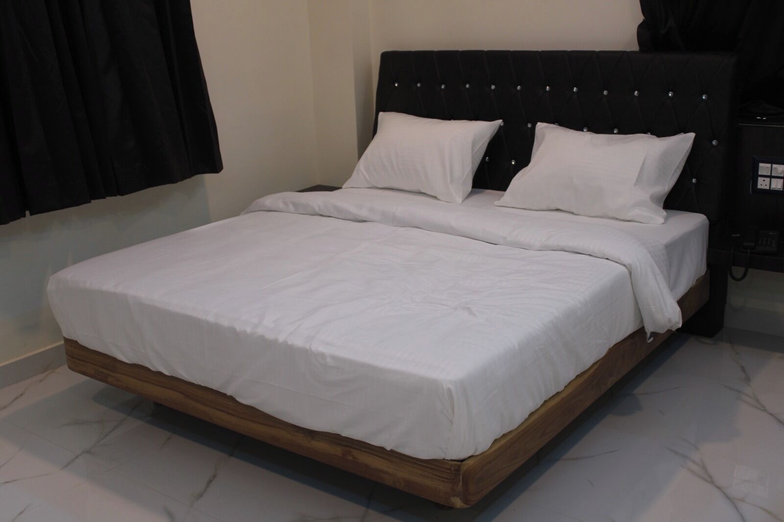 Ein Bett mit Holzrahmen und weißer Bettwäsche, ein schwarzer Kopfteil und ein kleiner Nachttisch mit Telefon.