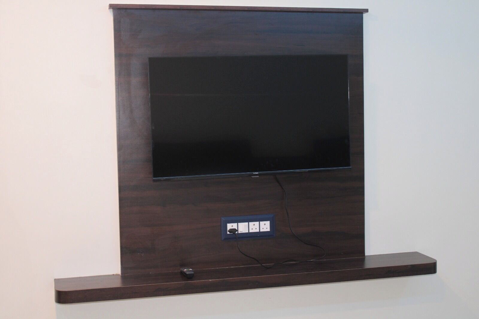 Televisor de pantalla plana montado en una pared de madera oscura con un enchufe debajo.