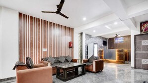 A modern lobby with a sofa set, a coffee table, a reception desk, and a ceiling fan. - Classic Green Residency (New Delhi)