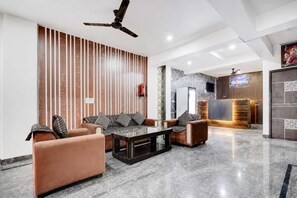 A modern lobby with a sofa set, a coffee table, a reception desk, and a ceiling fan. - Classic Green Residency (New Delhi)