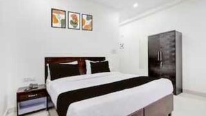 A hotel room with a bed, a wardrobe, a nightstand, and a wall-mounted shelf. - Classic Green Residency (New Delhi)