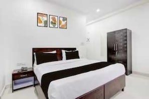 A hotel room with a bed, a wardrobe, a nightstand, and a wall-mounted shelf. - Classic Green Residency (New Delhi)