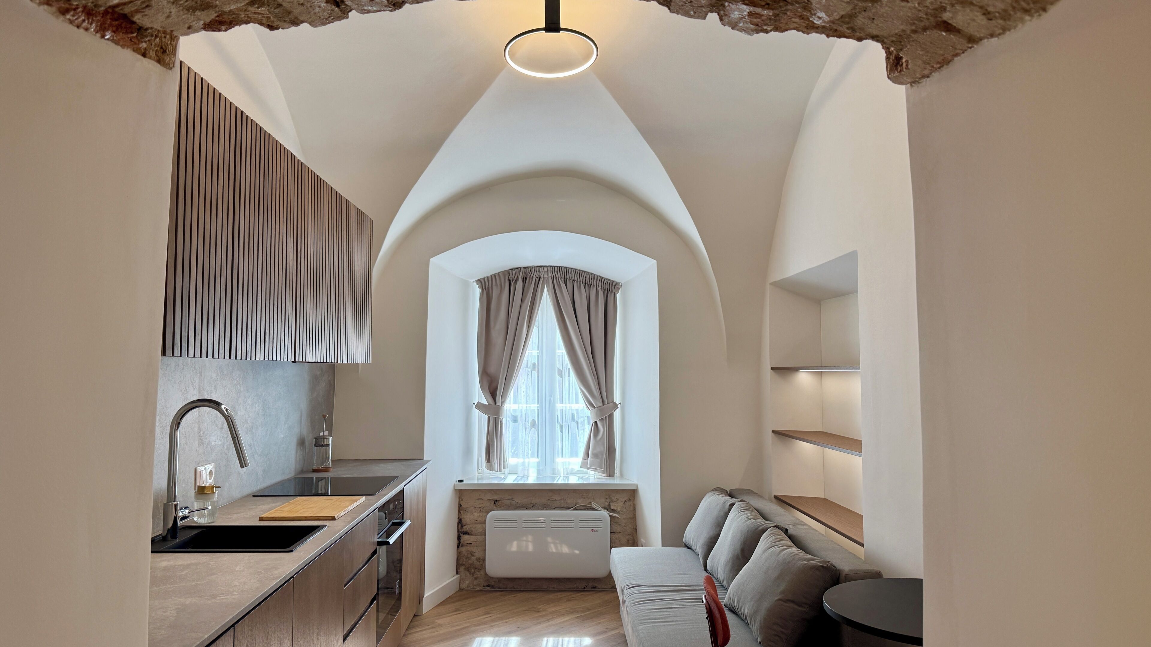 A modern kitchen with a built-in oven, a sink, and a window with curtains.