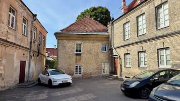 A narrow street with two parked cars, one white and one black, between old buildings with red-tiled roofs and brick facades.