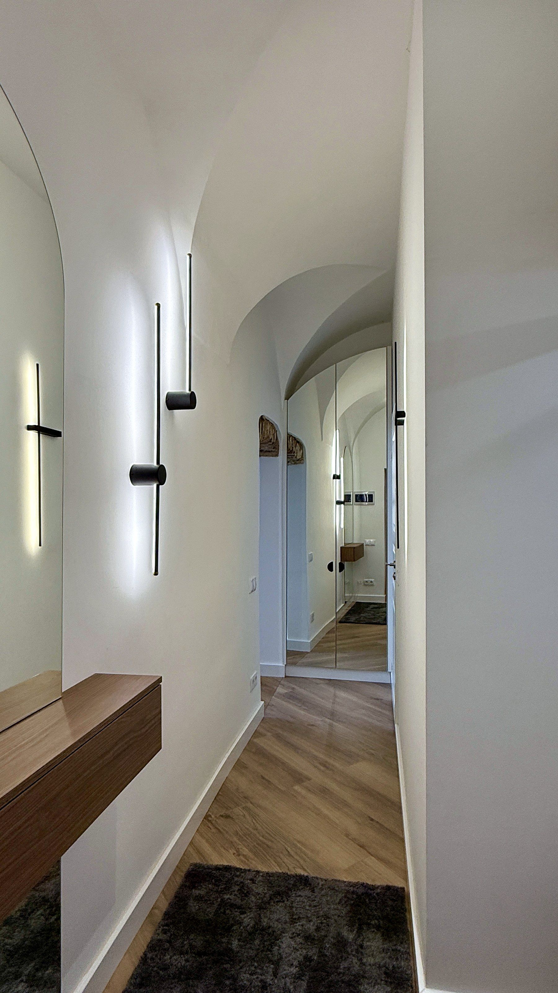 A hallway with a wooden bench, a dark rug, and a mirror reflecting the space.