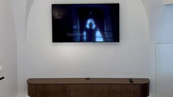 Un dormitorio con una televisión montada en una pared abovedada, una cama con cabecera de madera y una lámpara de techo moderna.