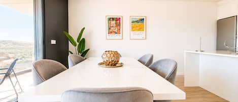 A modern dining area with a white table, grey chairs, and two framed artworks on the wall.