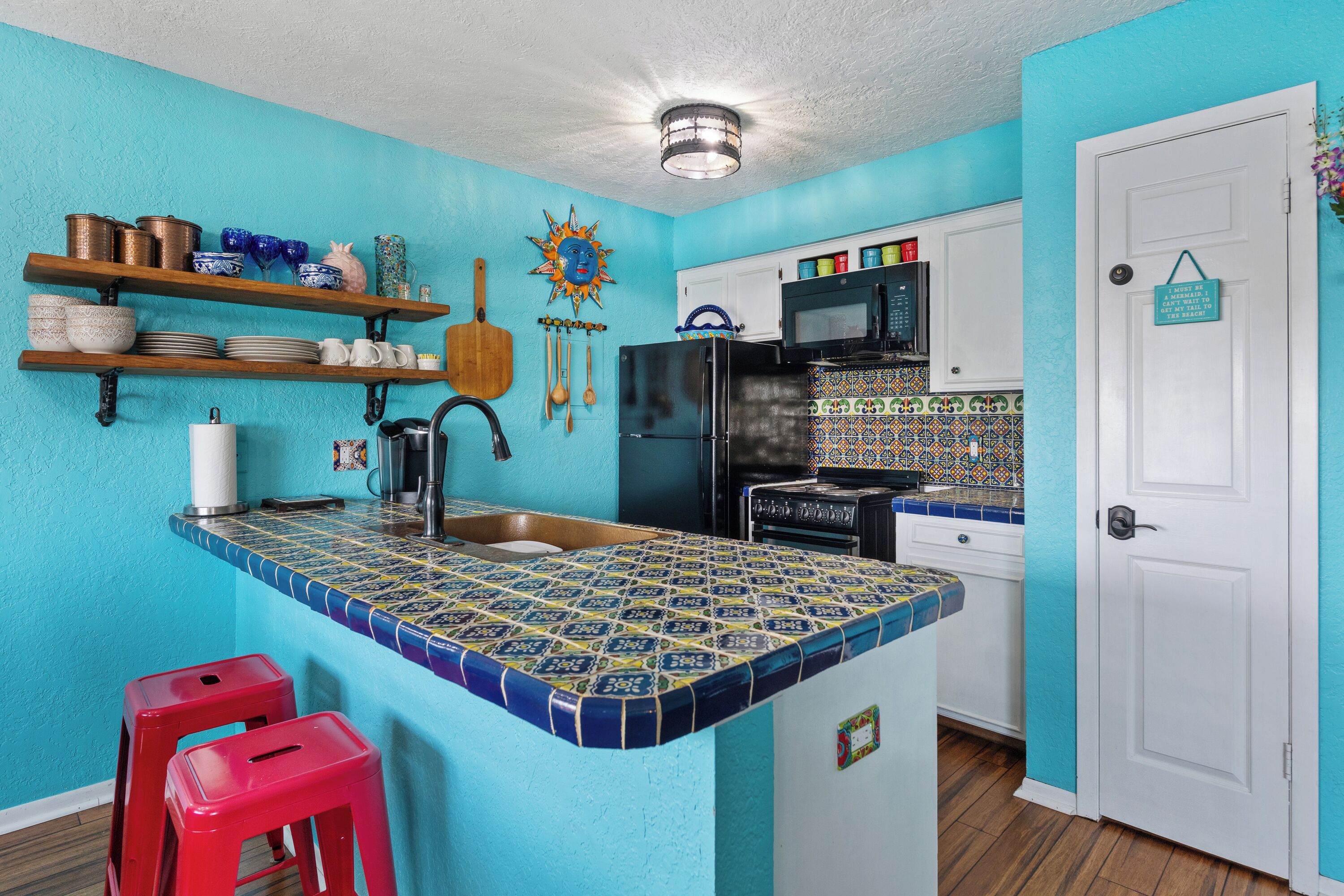 Una cocina con una isla azul con azulejos, estantes de madera, un refrigerador, un microondas y una estufa.