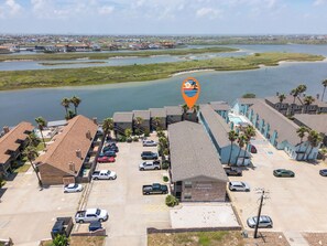 Een hotel aan de kust met een parkeerplaats, een gebouw met de naam 'Pirates Crossing' en uitzicht op het water en de verre skyline.
