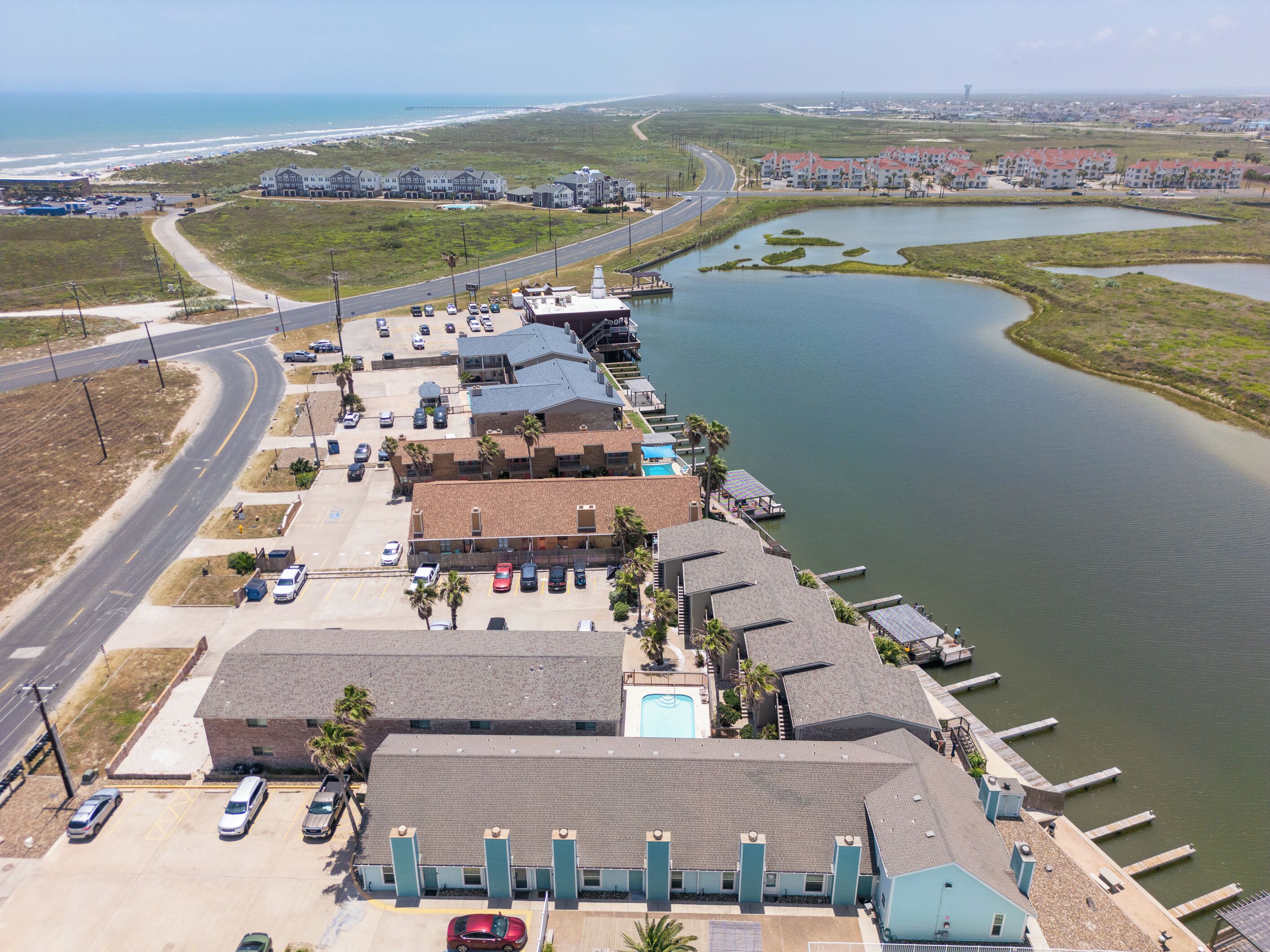 A coastal hotel with a swimming pool, parking area, and a view of the ocean.