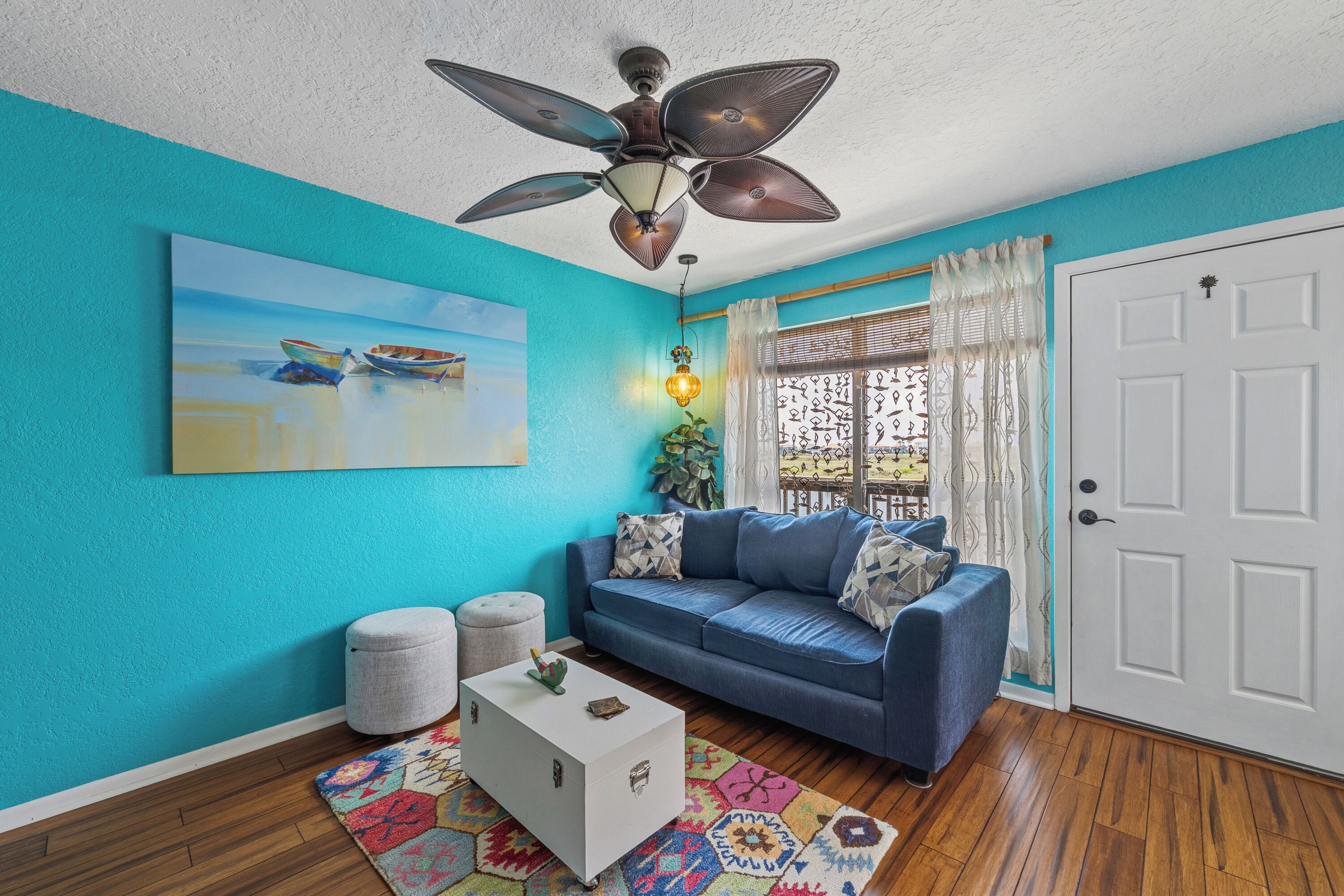 A living room with a blue wall, a ceiling fan, a sofa, a coffee table, and a painting of boats.