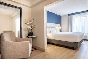 A hotel room with a bed, a chair, a small table, and a potted plant.