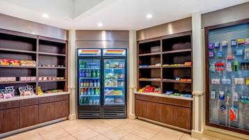 A hotel room with a minibar, a refrigerator stocked with beverages and snacks, and shelves with toiletries.
