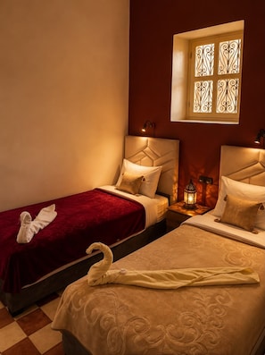 Quarto de hotel com duas camas, uma janela com vidro decorativo e uma mesa de cabeceira com um candeeiro.