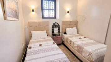 Une chambre à coucher avec deux lits, chacun doté d’une tête de lit, d’une table de chevet, d’un miroir et d’une fenêtre ornée de barreaux en fer décoratifs.