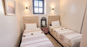 Quarto com duas camas, cada uma com cabeceira, mesa de cabeceira, espelho e janela com grades de ferro decorativas.