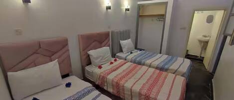 A hotel room with two beds, each with a distinct headboard design, a bedside table, and a wall-mounted light fixture.
