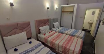 Habitación de hotel con dos camas, cada una con un diseño de cabecera diferente, una mesita de noche y una lámpara de pared.