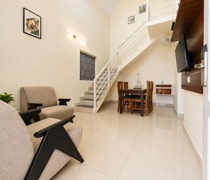 A modern living room with a sofa, a dining table, and a staircase leading to an upper floor.