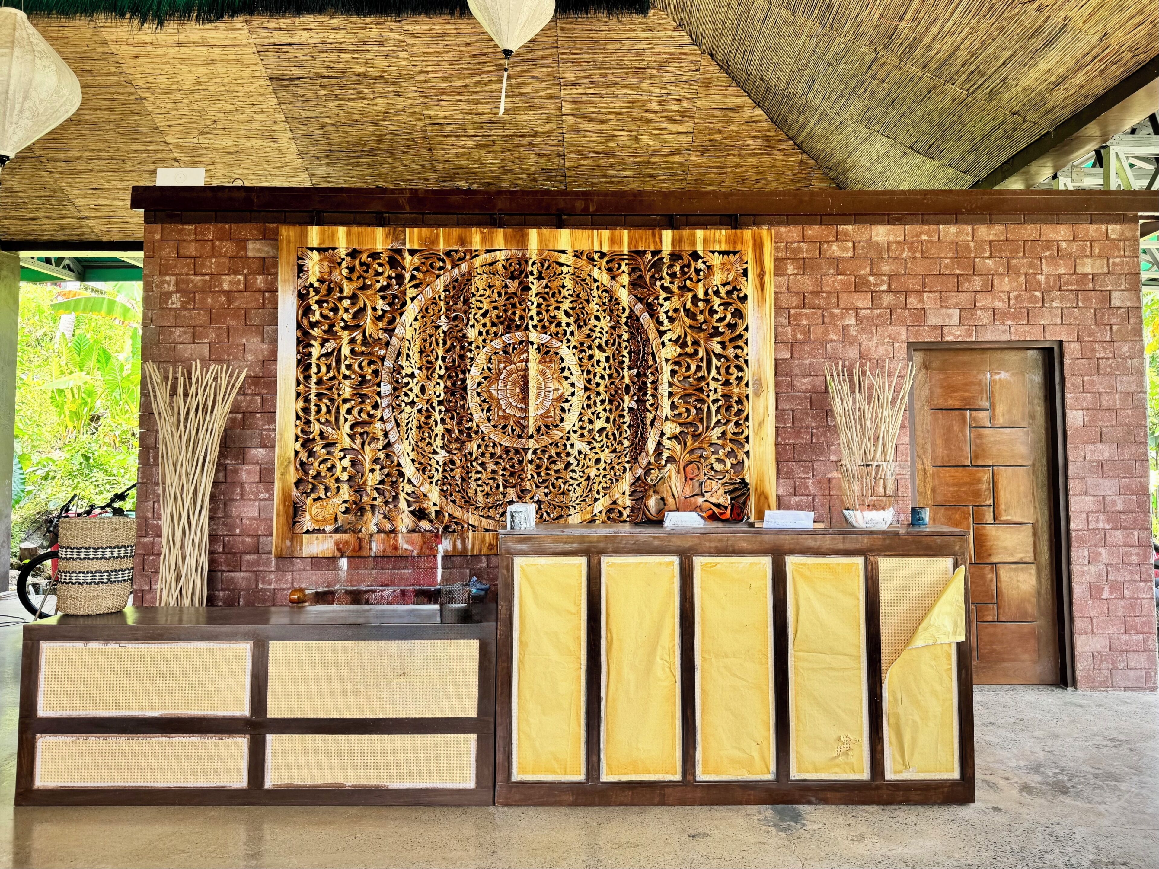 A reception area with a decorative wooden panel, a reception desk with woven panels, and a door with a textured design.