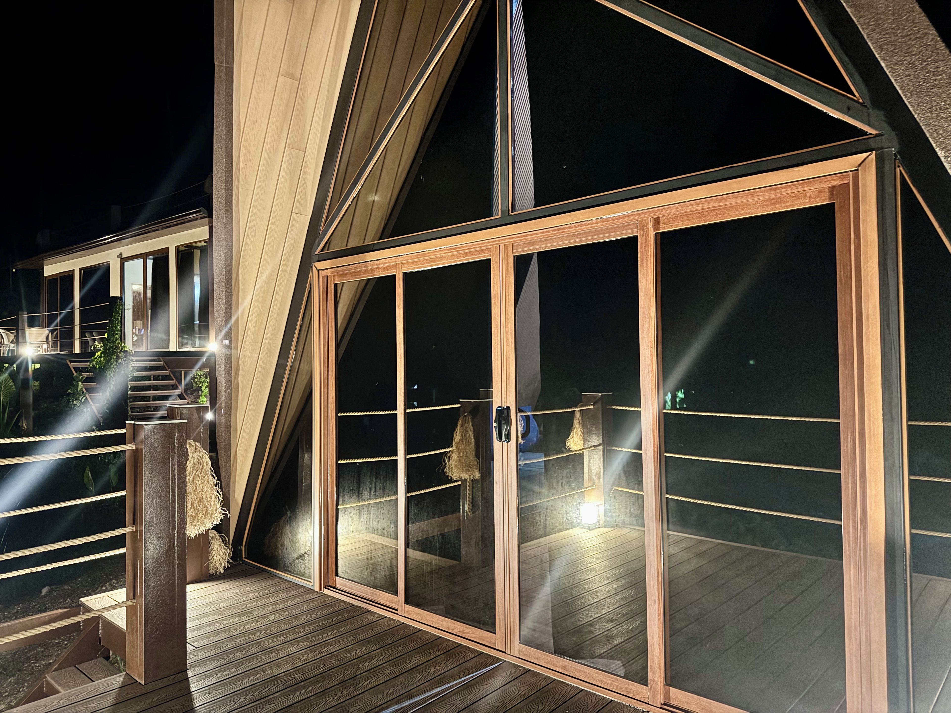 Un bâtiment moderne doté d’une terrasse en bois, de grandes fenêtres en verre et d’un escalier menant à un niveau supérieur.