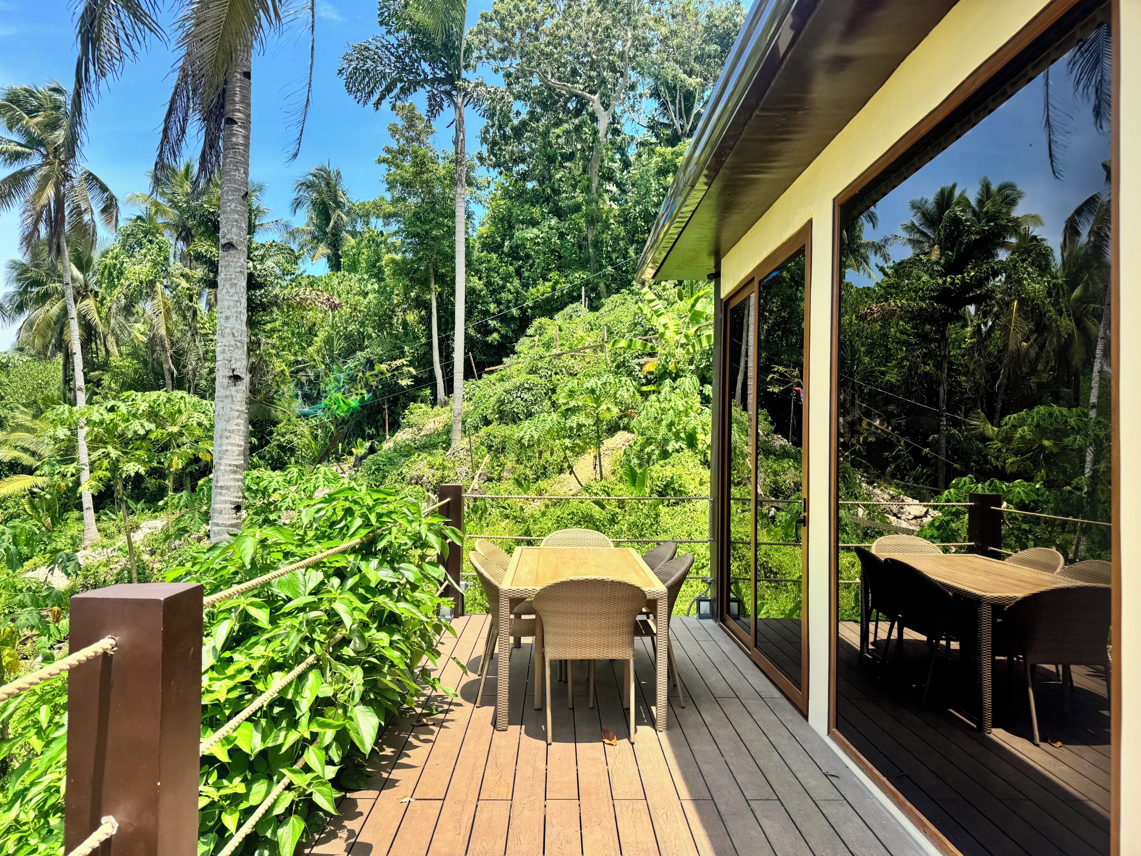 A wooden deck with wicker furniture, surrounded by lush greenery and tall trees.