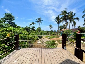 A wooden deck with rope barriers, overlooking a lush landscape with palm trees and a dirt path.