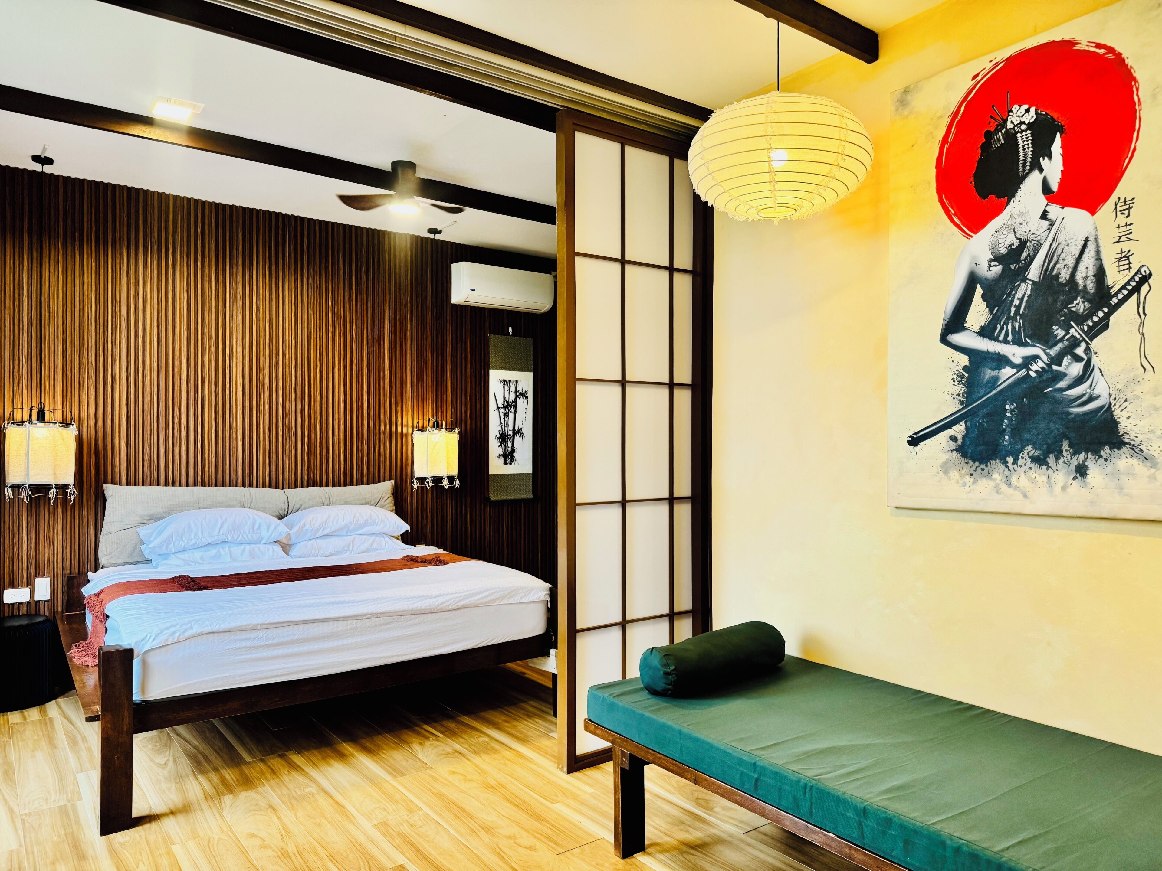 Una habitación con cama, mesita de noche, lámpara, un cuadro en la pared y un banco.