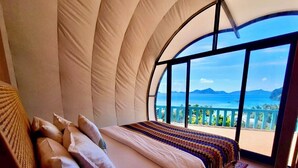 Ein Schlafzimmer mit einem großen, bogenförmigen Fenster mit Blick auf das Meer und die Berge.