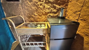 Uma cozinha compacta com geladeira, fogão pequeno e uma cesta de vime com copos.