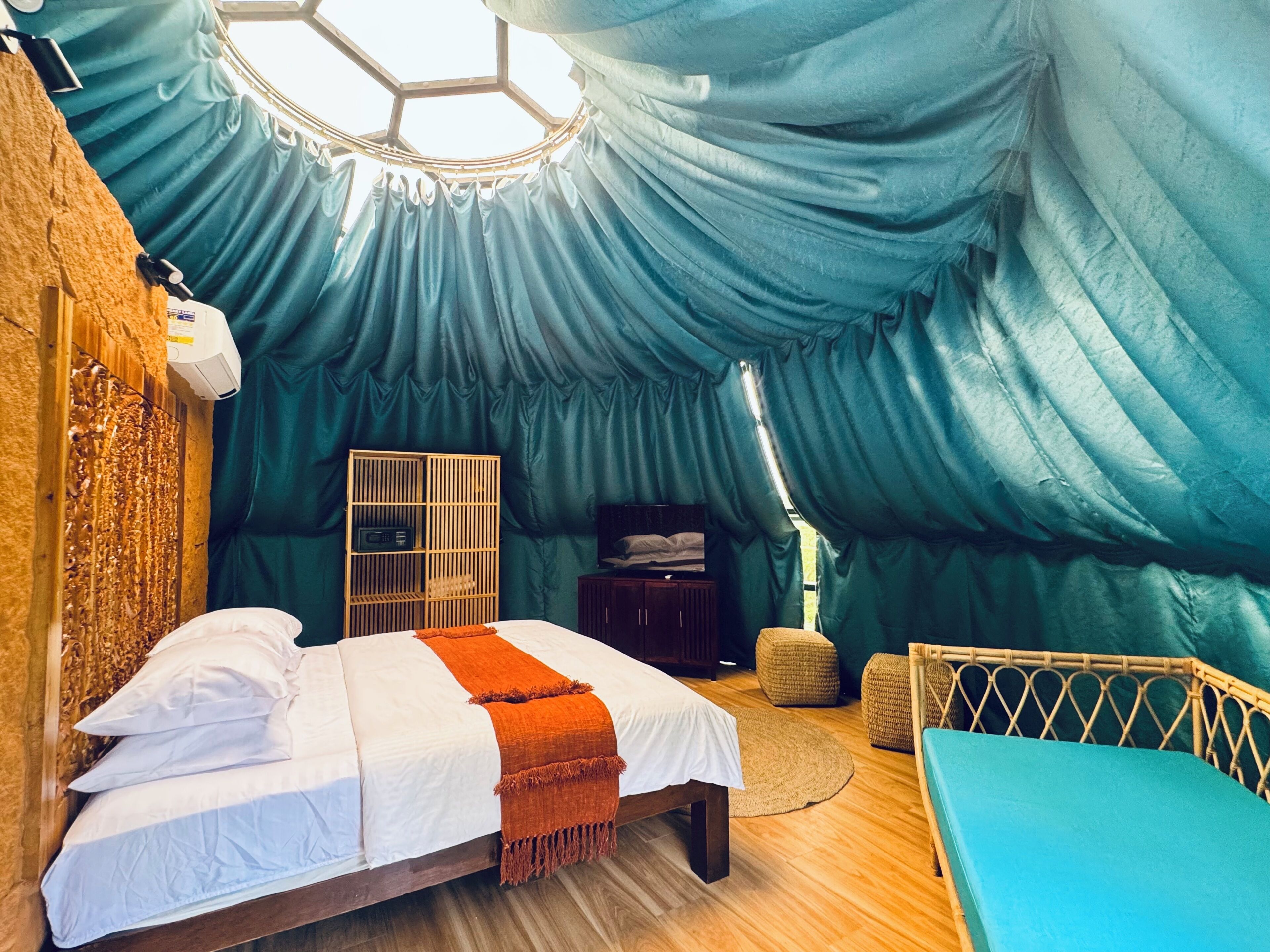 A cozy, tent-like room with a bed, a small wooden cabinet, and a round table.