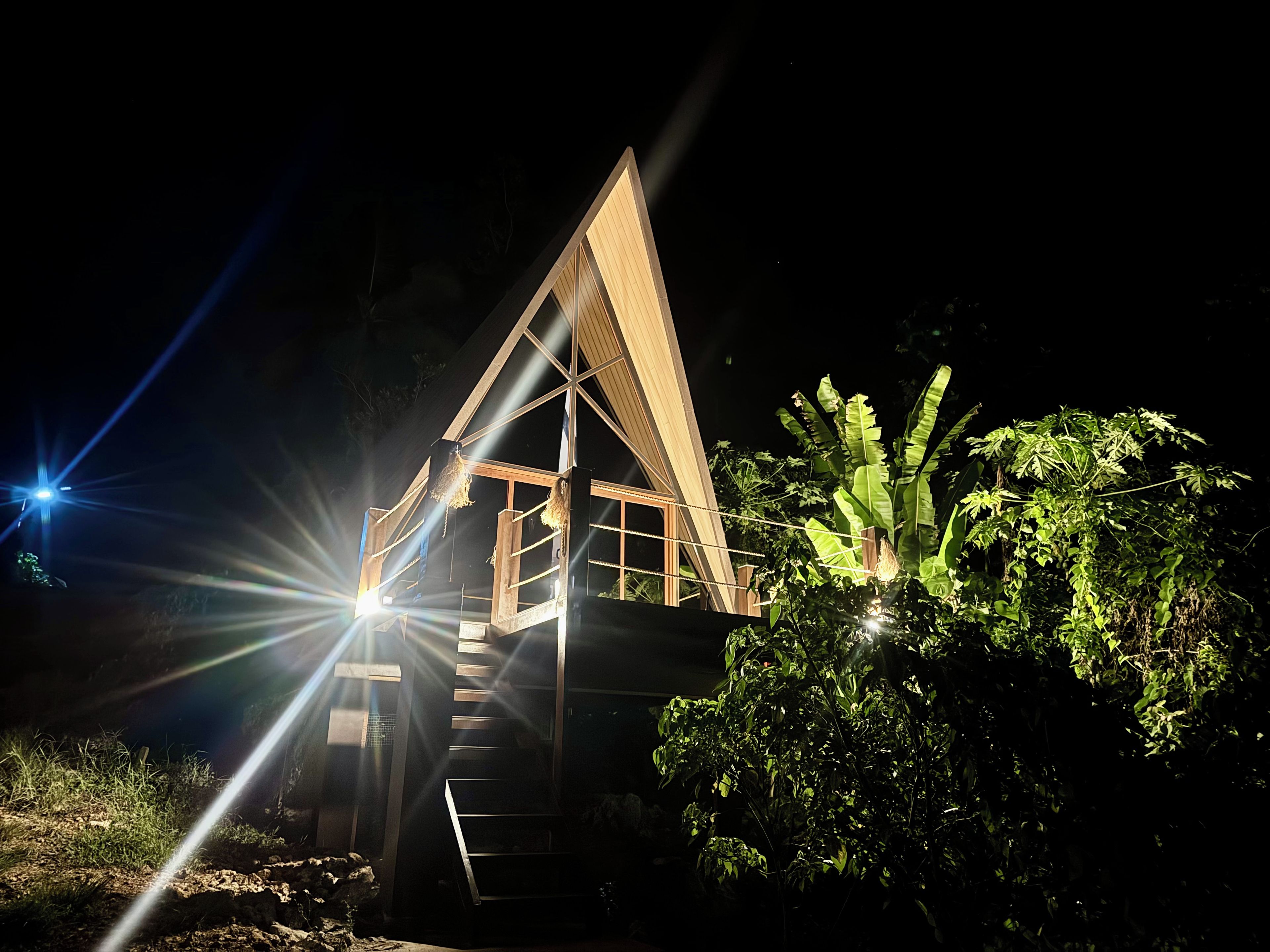 A triangular wooden structure with a staircase leading to an upper level, surrounded by vegetation.