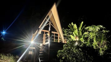 A triangular wooden structure with a staircase leading to an upper level, surrounded by vegetation.