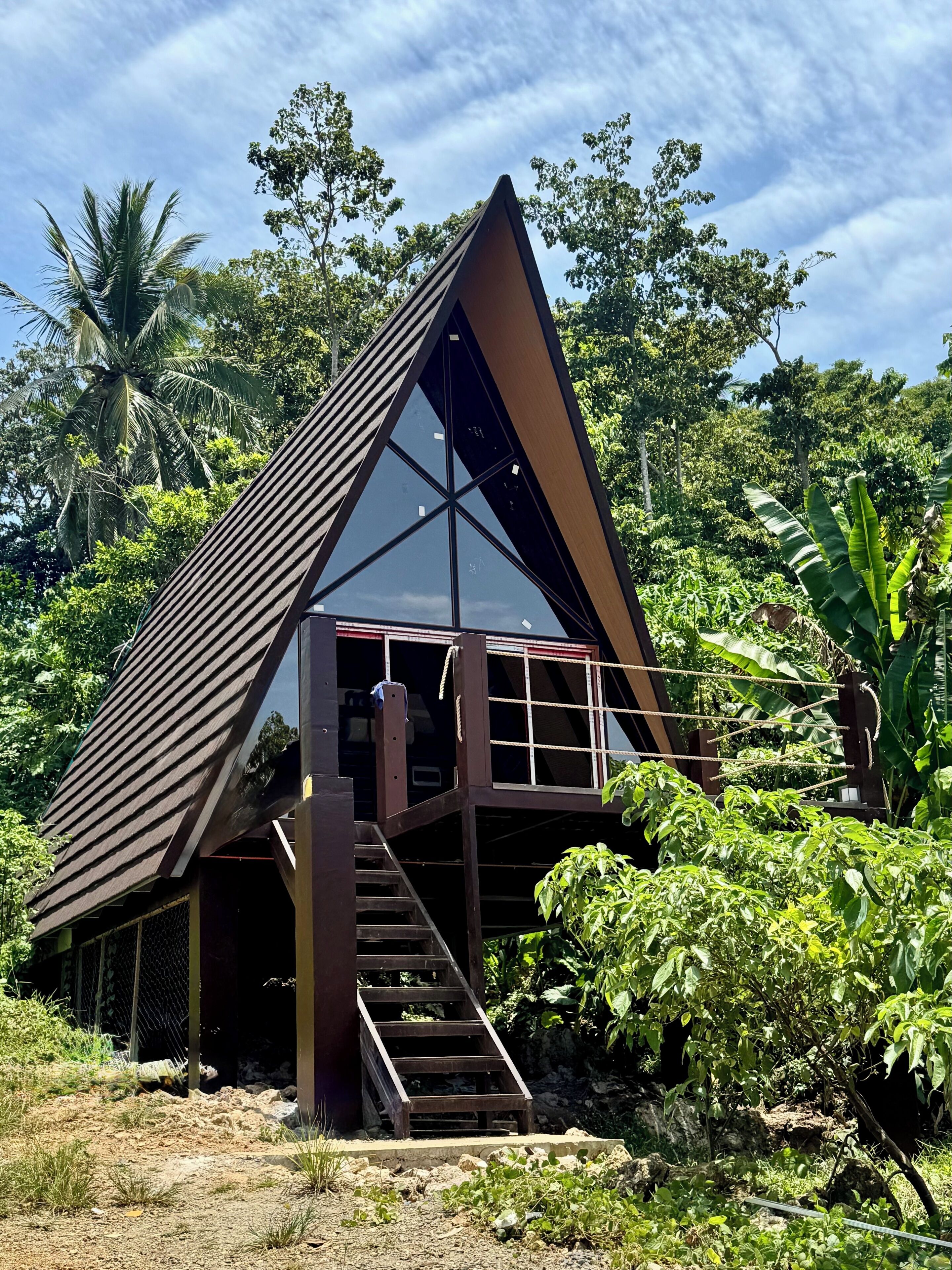 A triangular building with a wooden exterior and a glass facade, surrounded by lush greenery.