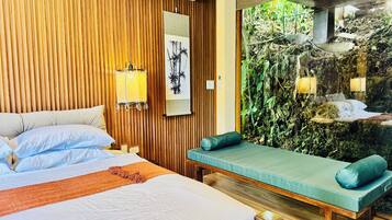 A hotel room with a bed, a bench, a wall-mounted air conditioner, and a large window with a view of a rocky garden.