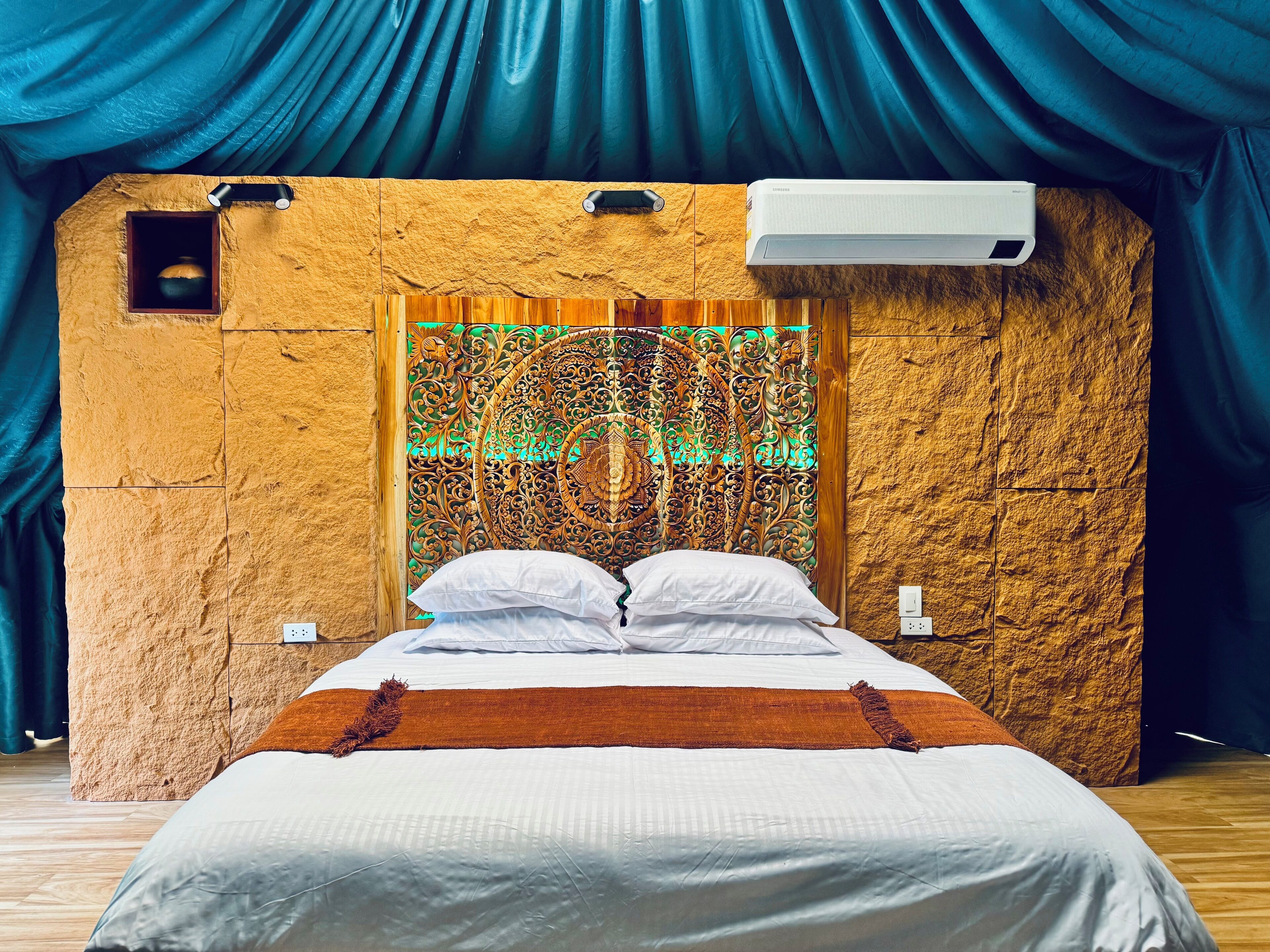 Una cama con sábanas blancas, un plaid marrón y un cabecero decorativo con diseños intrincados.