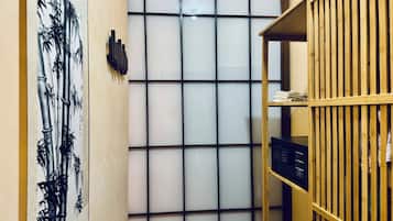 Una habitación con una obra de arte de bambú en la pared, un estante de madera con objetos y una ventana con diseño de cuadrícula.
