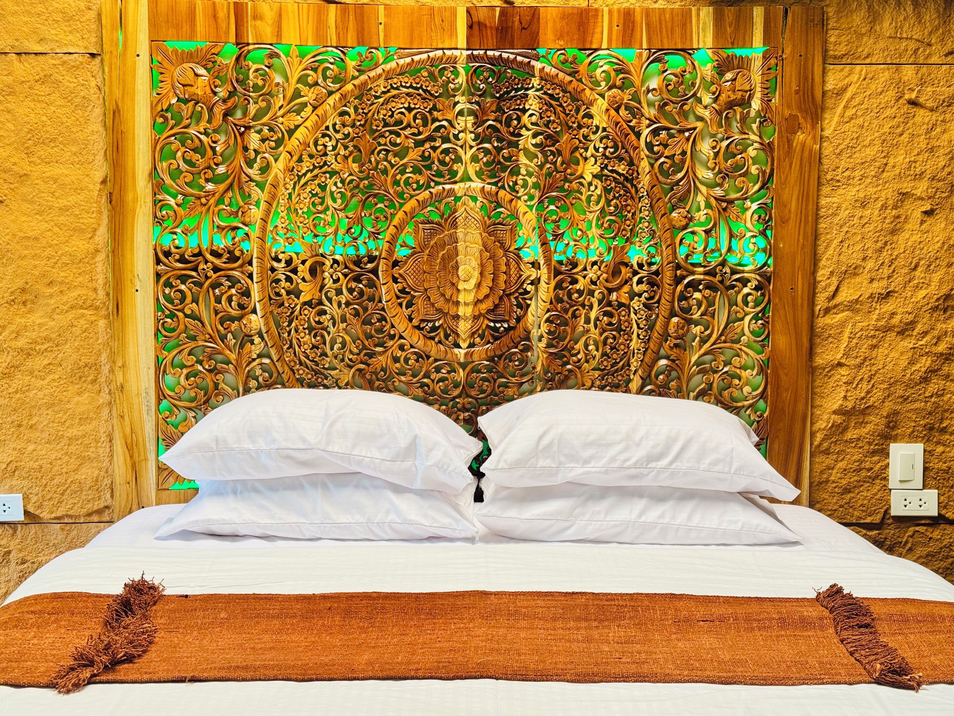 A bed with a headboard featuring intricate carvings, white pillows, and a brown throw blanket.