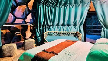 Una habitación con cama, ventana con cortinas, un ordenador portátil sobre un soporte y muebles de mimbre.