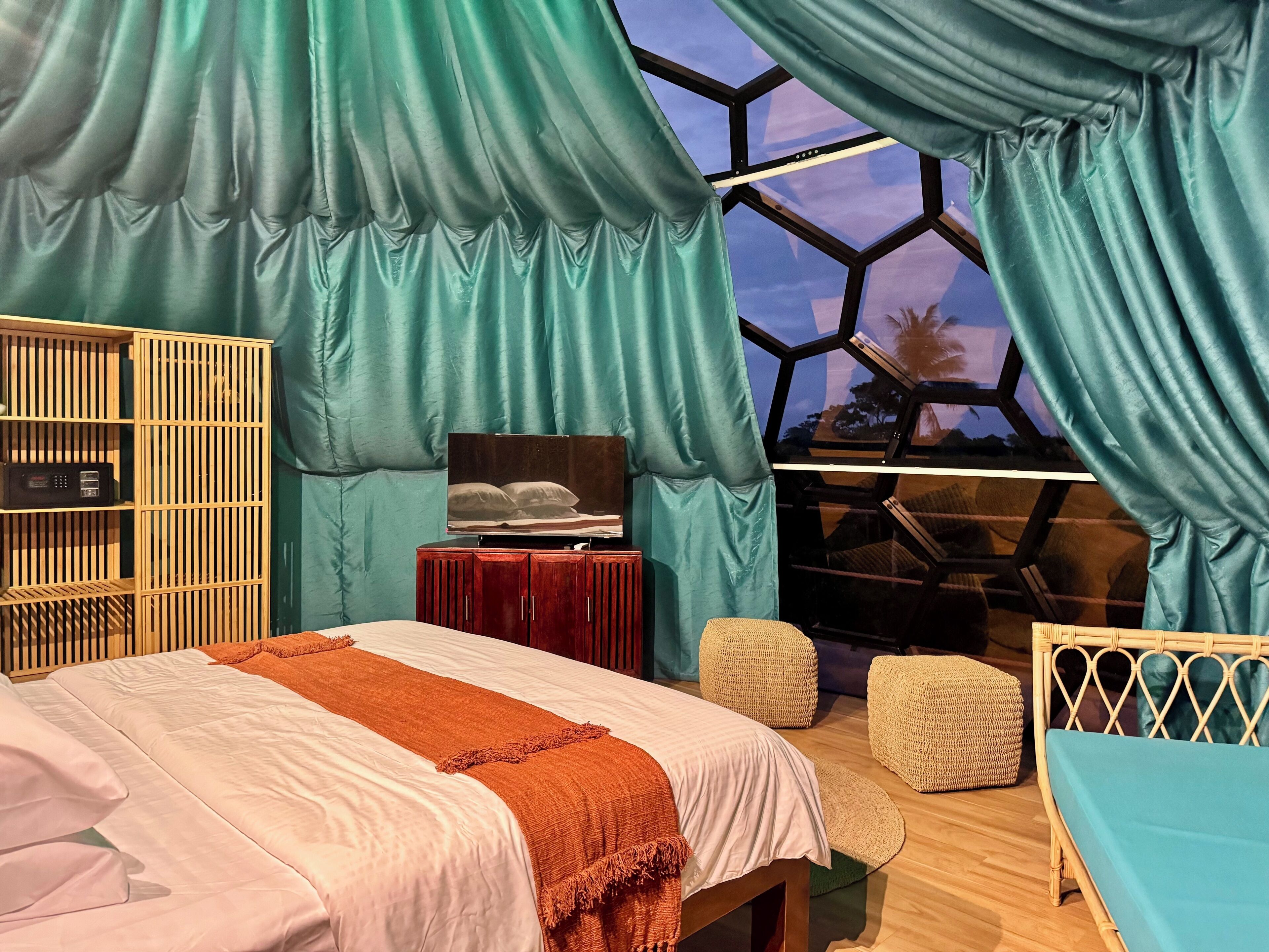 A bedroom with a bed, a TV, a wooden cabinet, and a window with curtains.