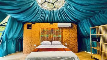 A room with a bed, a wooden floor, a wall with a hexagonal window, and a ceiling with draped fabric.