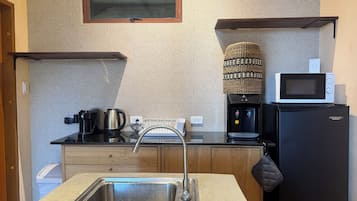 A compact kitchen with a stainless steel sink, a coffee maker, a kettle, a microwave, and a water dispenser.