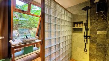 Une salle de bain avec une douche, un banc en bois et une fenêtre donnant sur un paysage verdoyant.