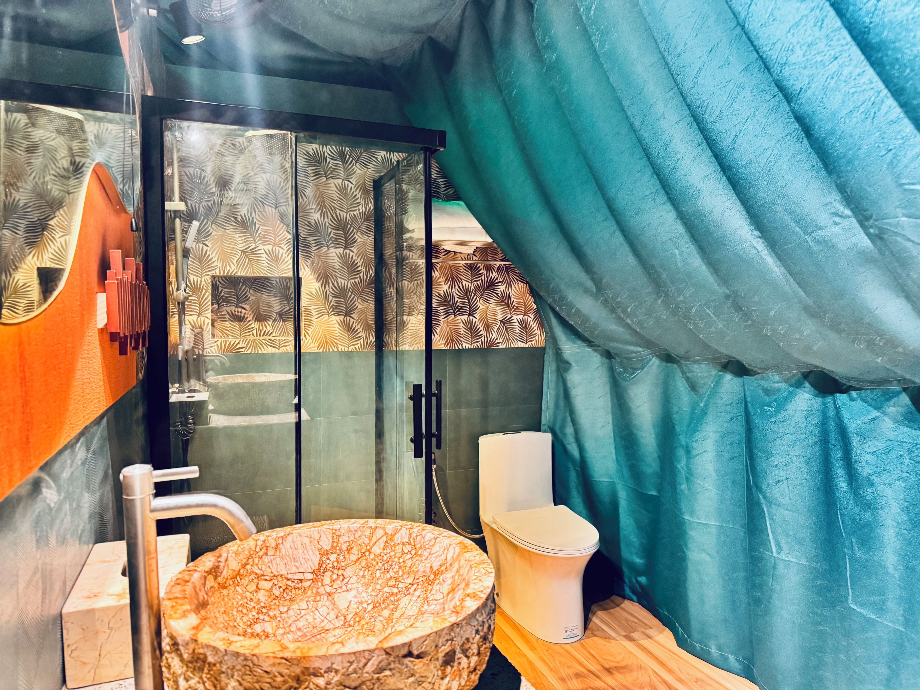 Un baño con lavamanos de mármol, inodoro y zona de ducha con puerta de vidrio.