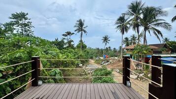 Una terraza de madera con barandas de cuerda, con vistas a un paisaje exuberante con palmeras y una estructura con techo de paja.