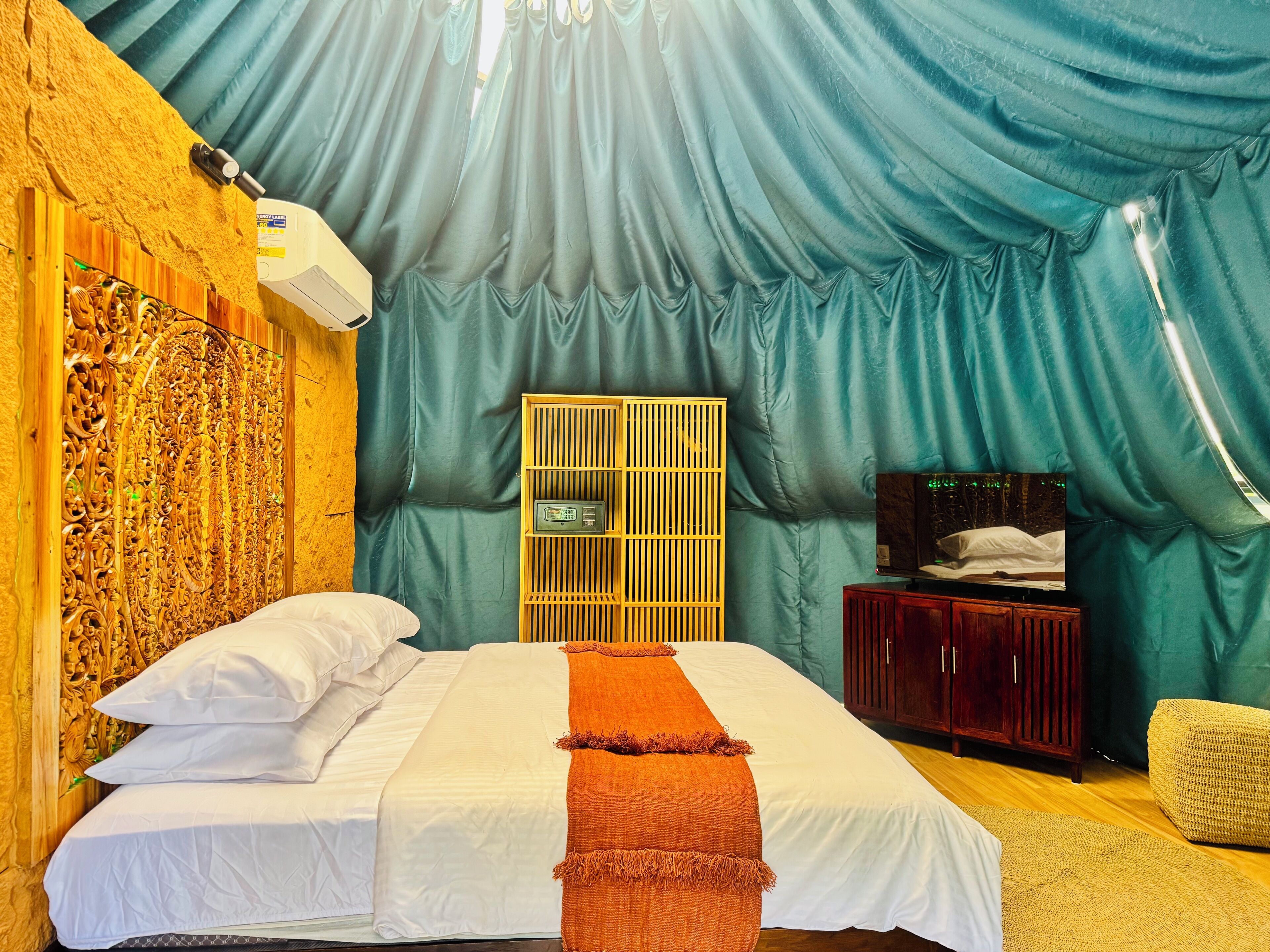 Una habitación con una cama, cabecero de madera, una radio, un armario y una cortina grande.