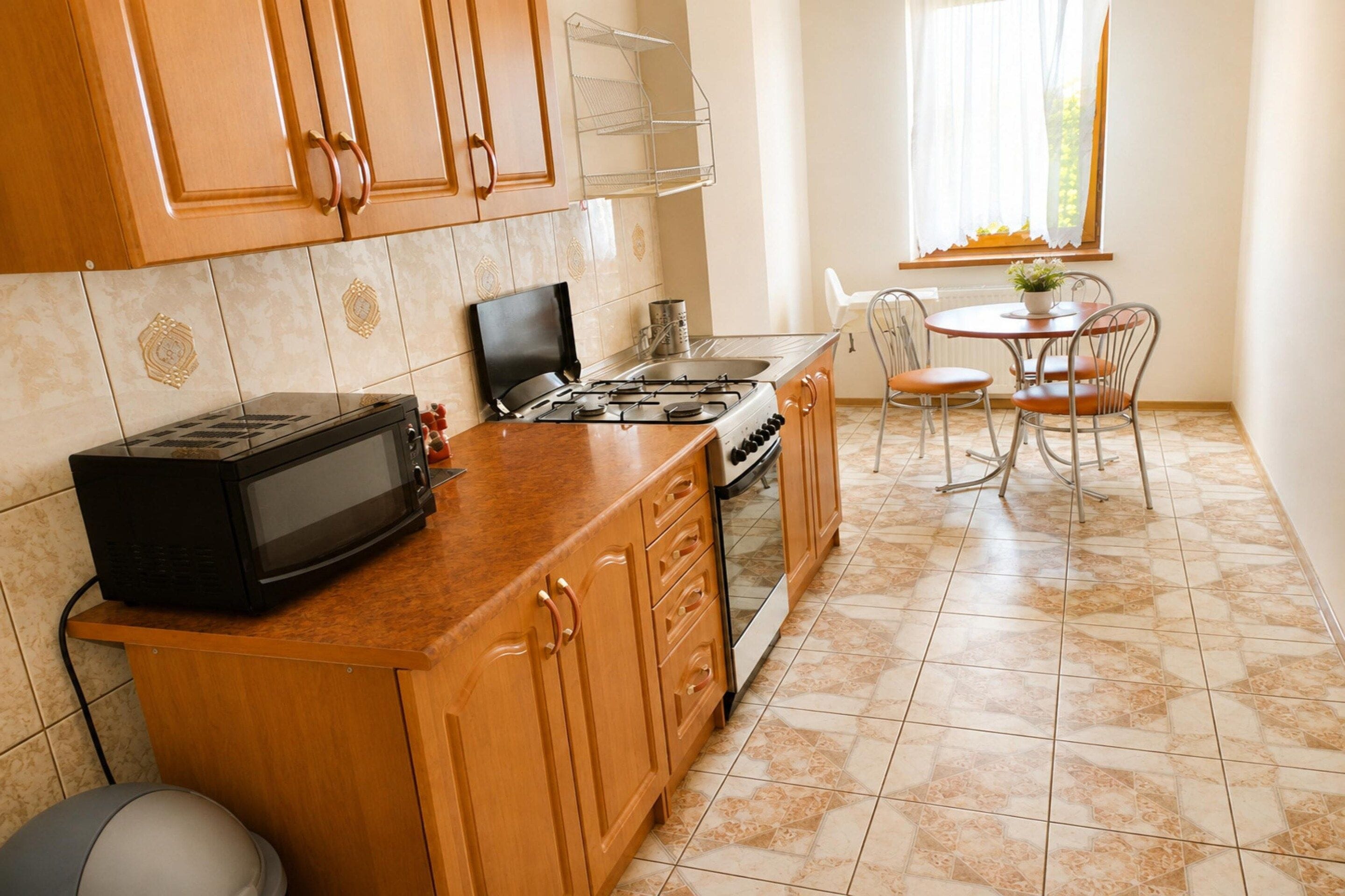 A kitchen with wooden cabinets, a stove, a microwave, and a dining area with a table and chairs.